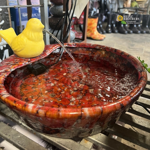 An orange bird bath with a yellow bird on top that has water flowing through it's beak