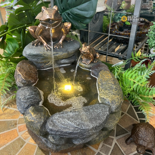 A stone bird bath with a bronze frog on top that has water flowing through it's mouth