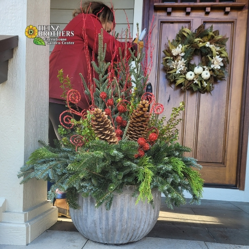 Holiday plants outside in a large gray planter in front of a door with a holiday wreath