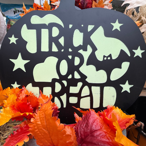 Halloween-themed decoration with 'Trick or Treat' text and bat design, surrounded by autumn leaves.