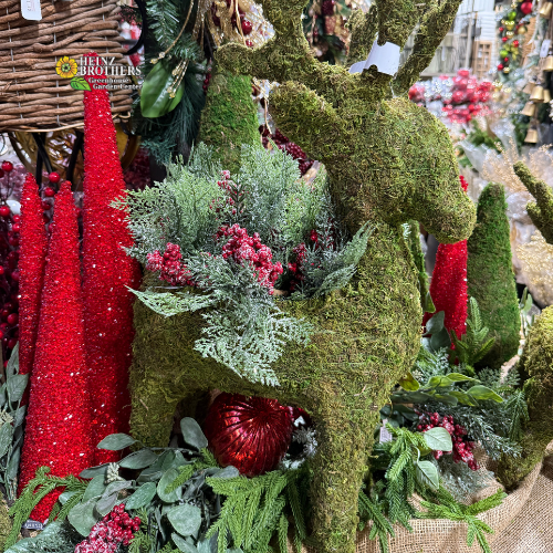 Decorative reindeer planter made of moss with red glitter trees and artificial garland and natural elements in a festive holiday setting.